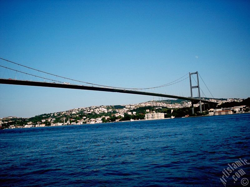 View of Bosphorus Bridge, Camlica Hill, Beylerbeyi coast and the moon seen in daytime over the bridge`s legs from Ortakoy shore in Istanbul city of Turkey.
